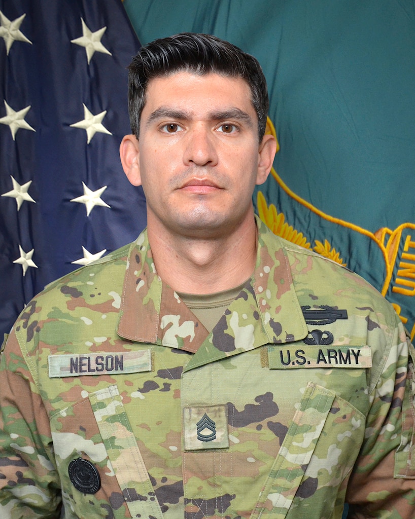 Man in U.S. Army uniform standing in front of two flags.
