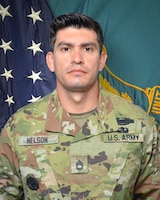 Man in U.S. Army uniform standing in front of two flags.