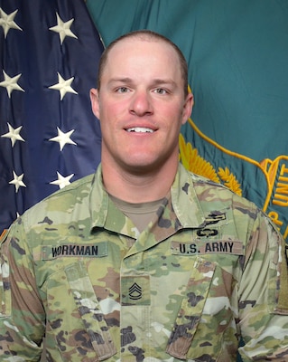 Man in U.S. Army uniform standing in front of two flags.