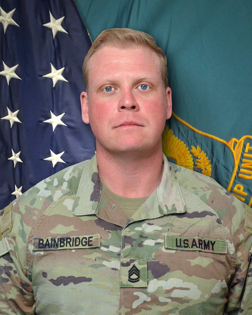 Man in U.S. Army uniform standing in front of two flags.