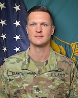 Man in U.S. Army uniform standing in front of two flags.