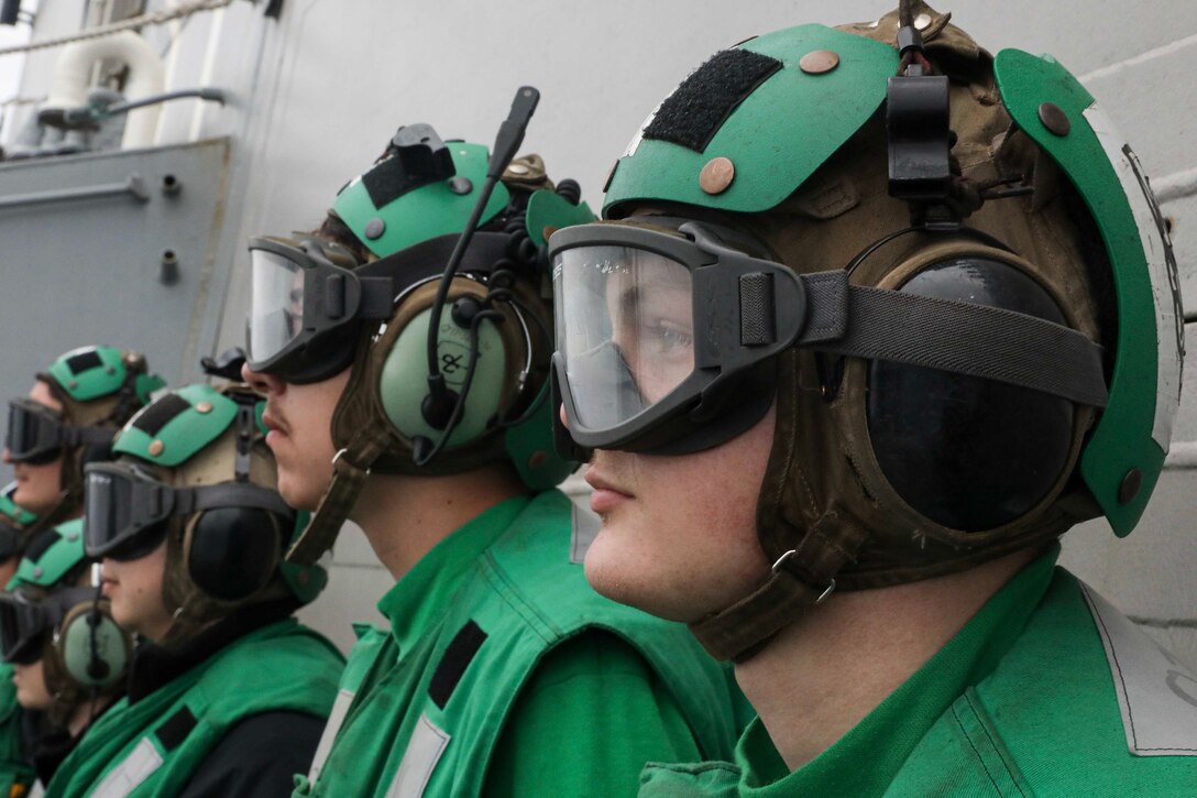 Sailors wearing goggles and headsets stand in a row.