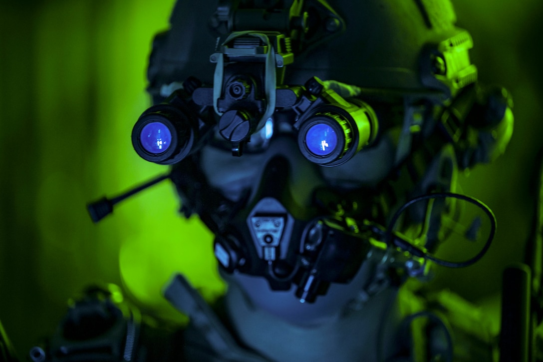 A close shot of an airman’s face wearing tactical gear illuminated by green light.