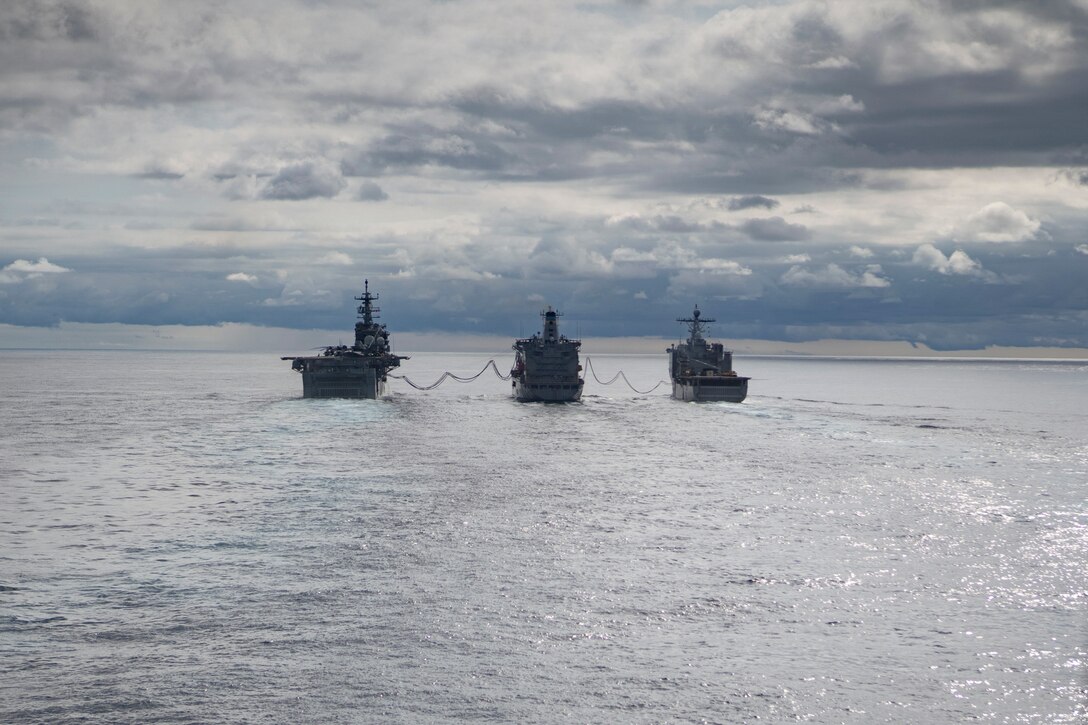 Three ships connected by fuel hoses sail in formation.