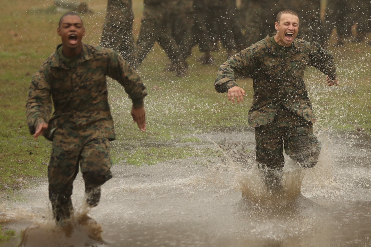 Two Marine Corps recruits scream as they run through a swamp.