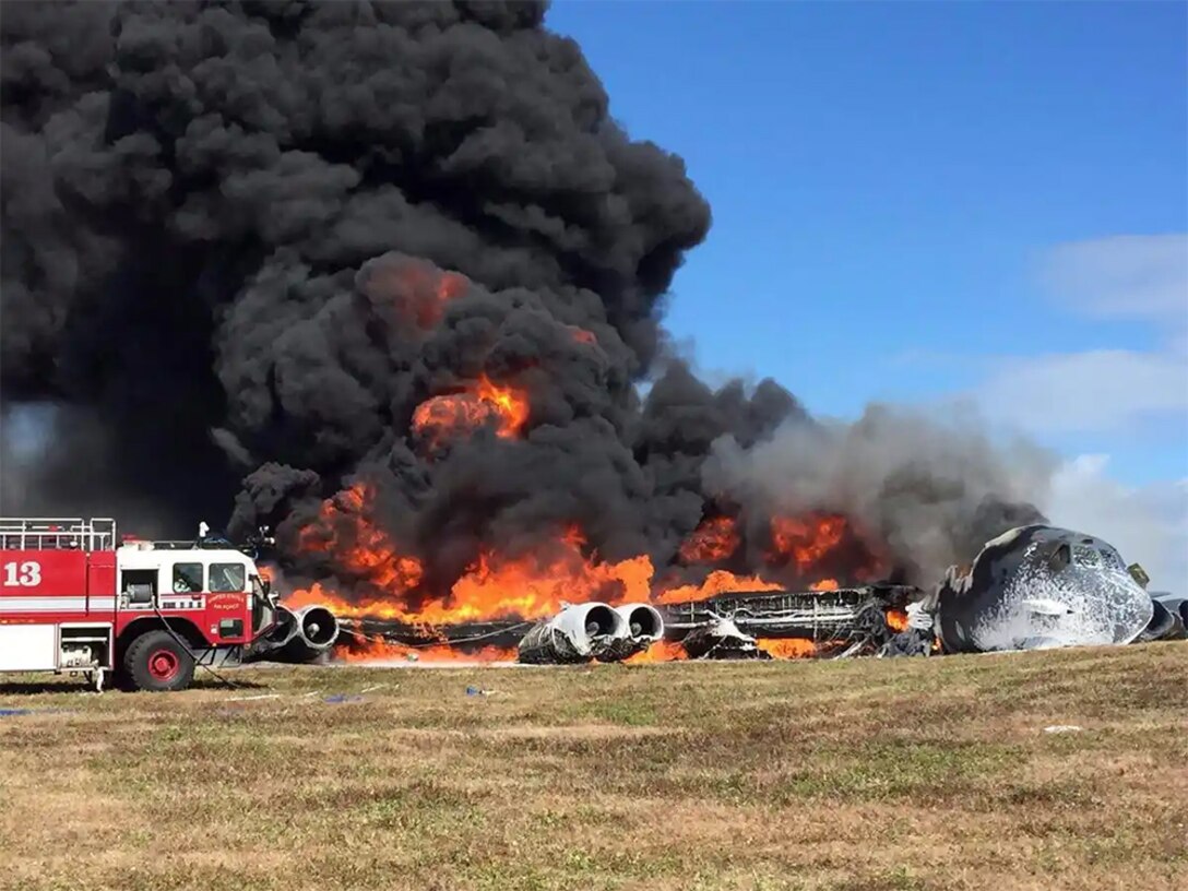 An airplane burns and a firetruck sits nearby.