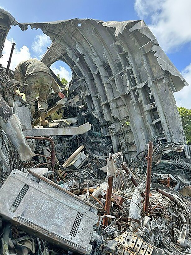 An airman clambers around in a torn apart airplane.