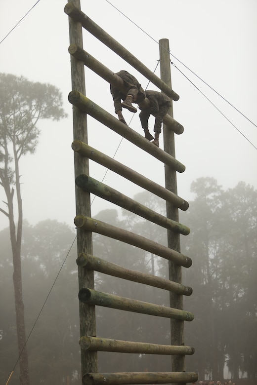 Two Marine Corps recruits climb a tall ladder.