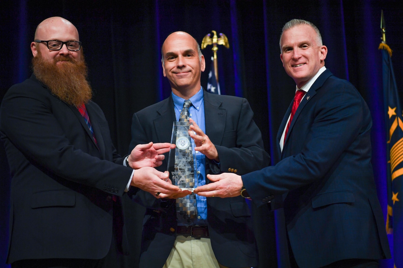 Three people are holding an award.