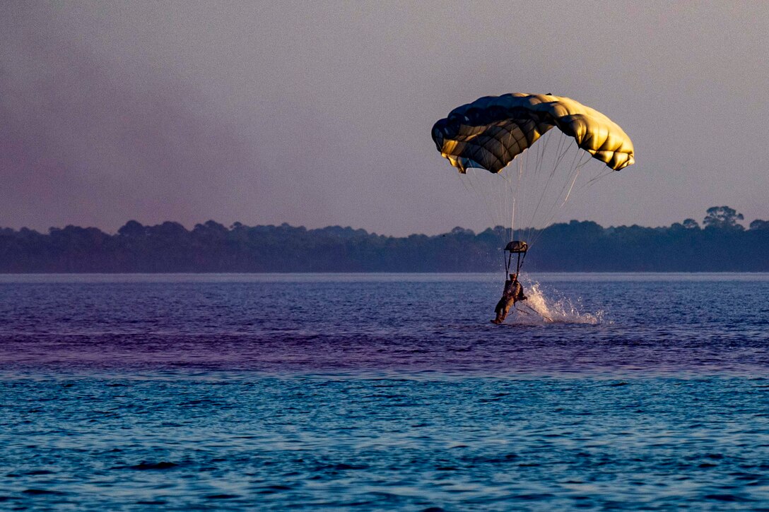 A sailor splashes while landing by parachute in water.