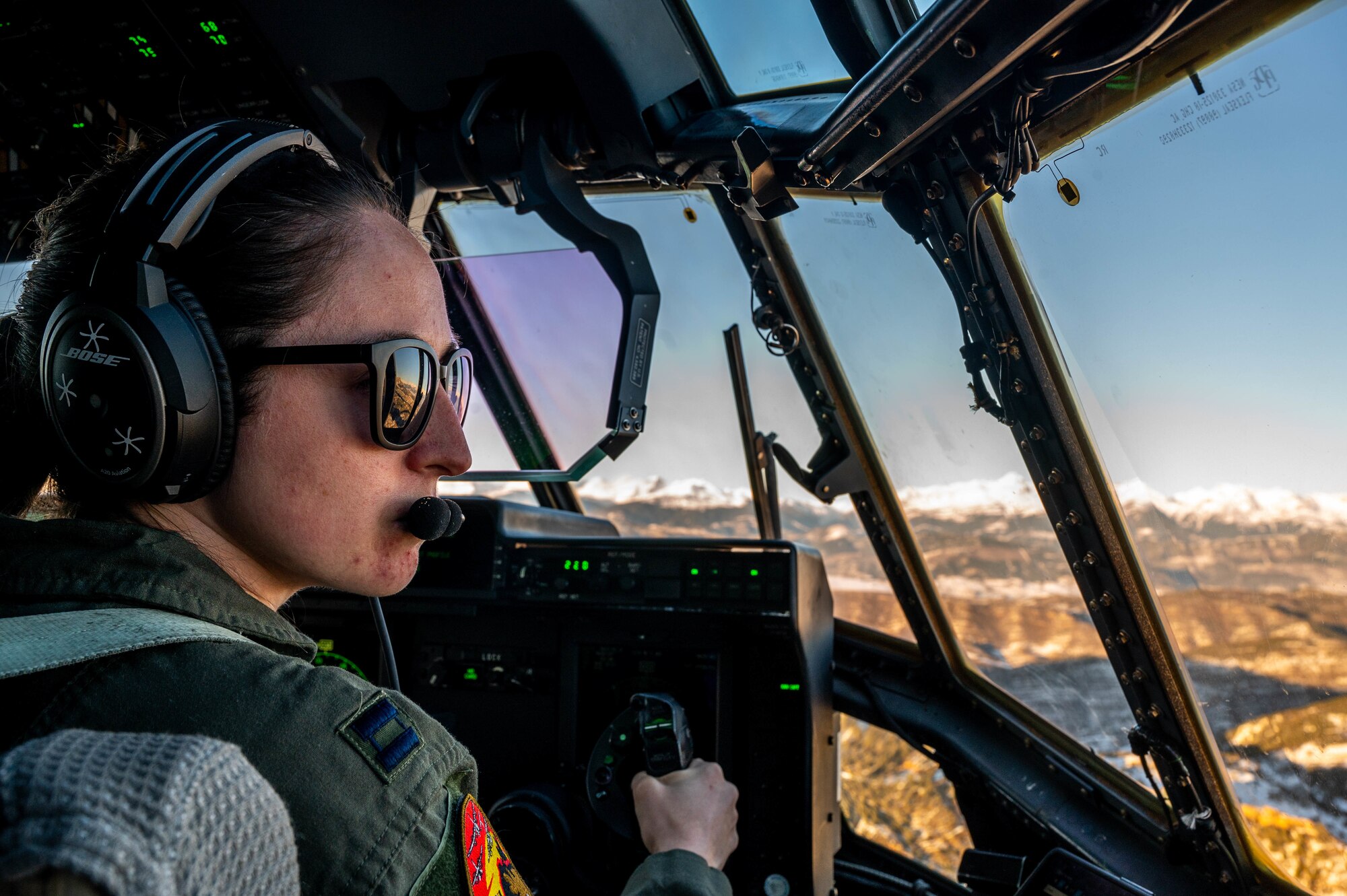 A pilot looks outside at mountains while flying a C-130J.