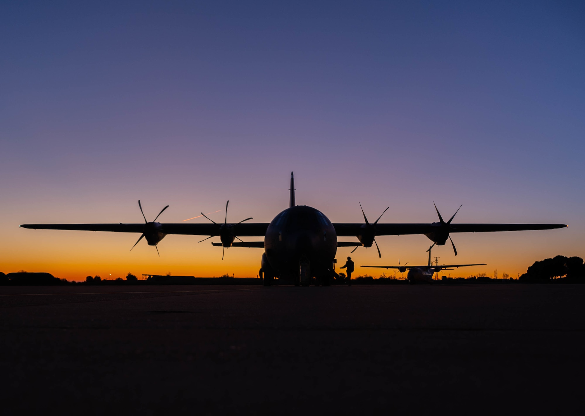 An aircraft is a silhouette against a purple, blue and orange sky.