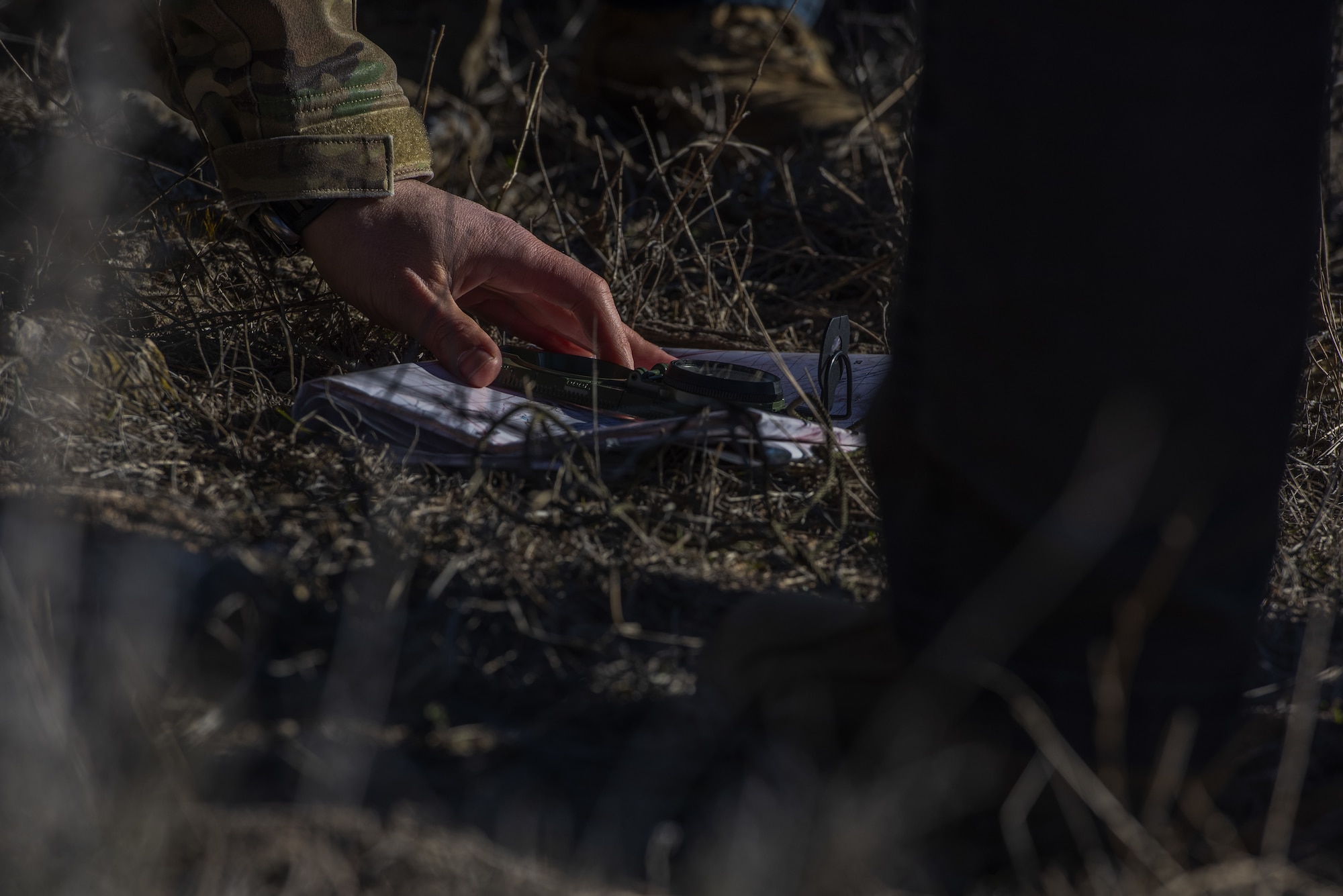 A man's hand is touching a compass and map on grass.