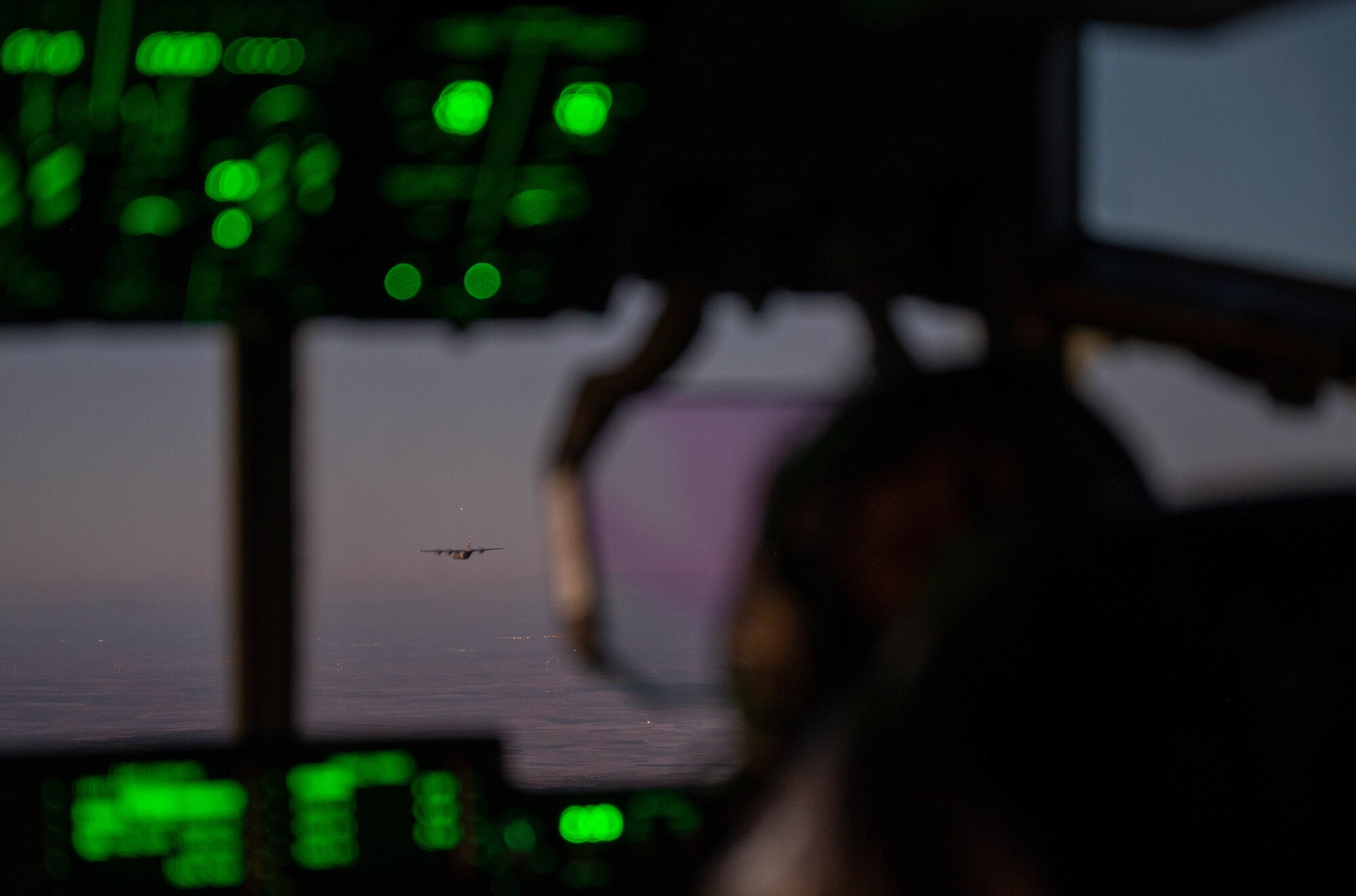 There is an aircraft that can be seen flying the in the air over blue water through the window of another aircraft.