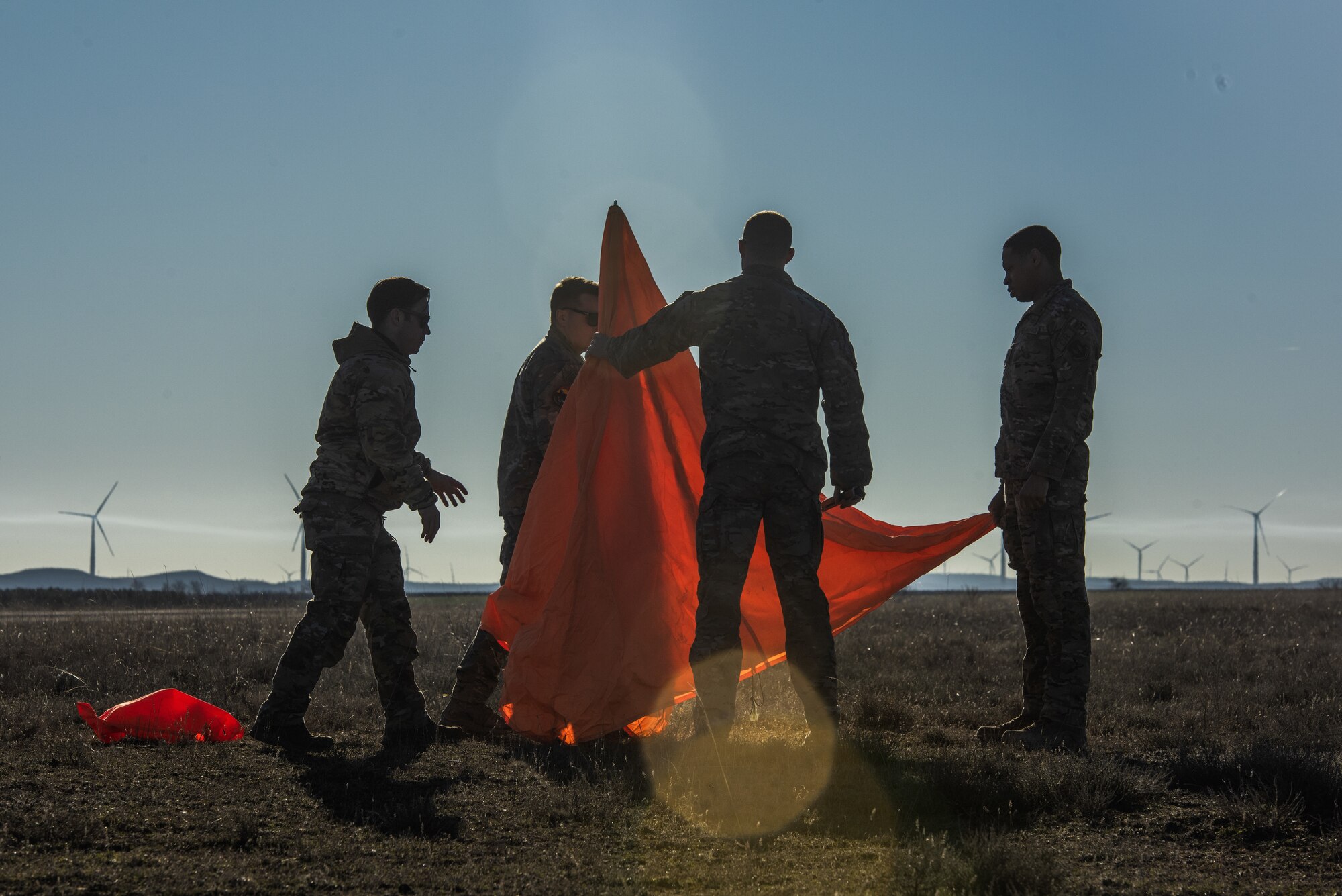 There are four people assembling an orange cone made of fabric. The sky is blue