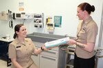 A Navy physician and corpsman standing wearing khaki uniforms standing together in a patient care room.