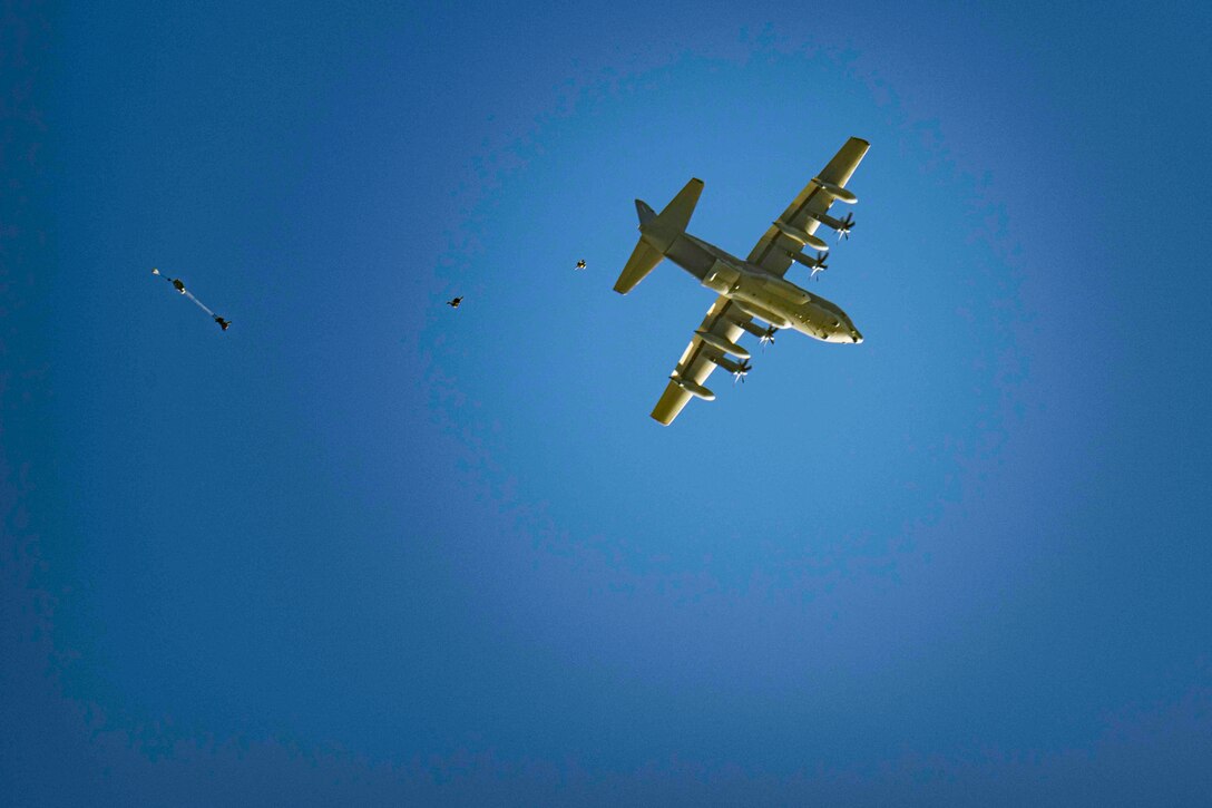 Sailors jump from an Air Force plane in blue sky.
