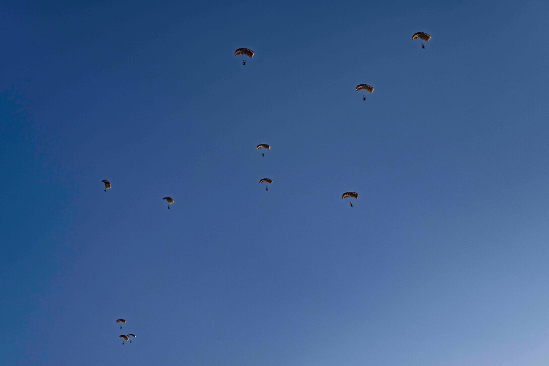 About 10 sailors parachute in blue sky.