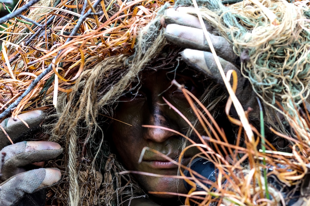 A soldier hides his face in rope fibers, sticks and other materials.