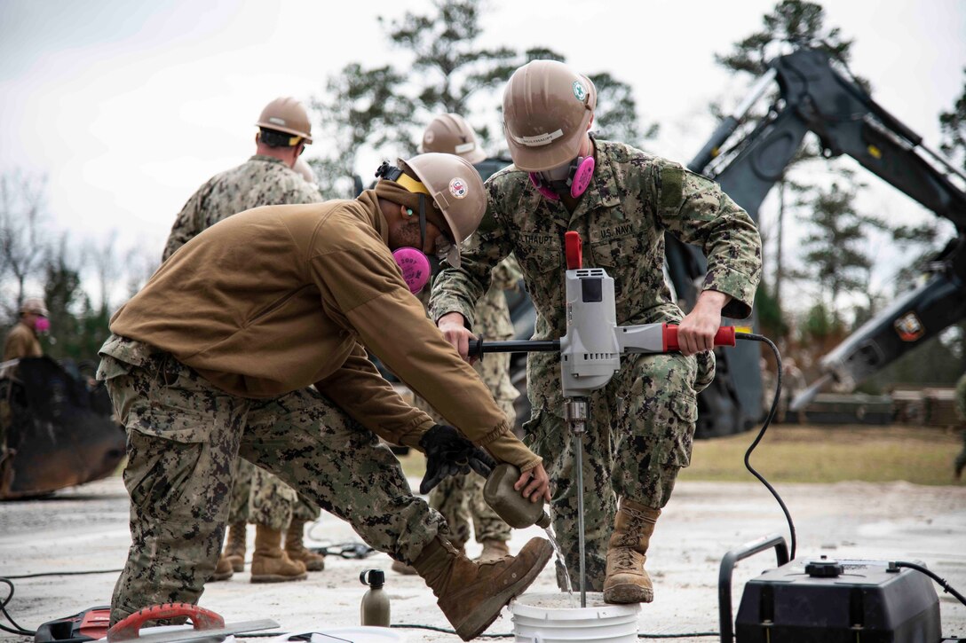 Two sailors use tools to mix concrete on an airfield.