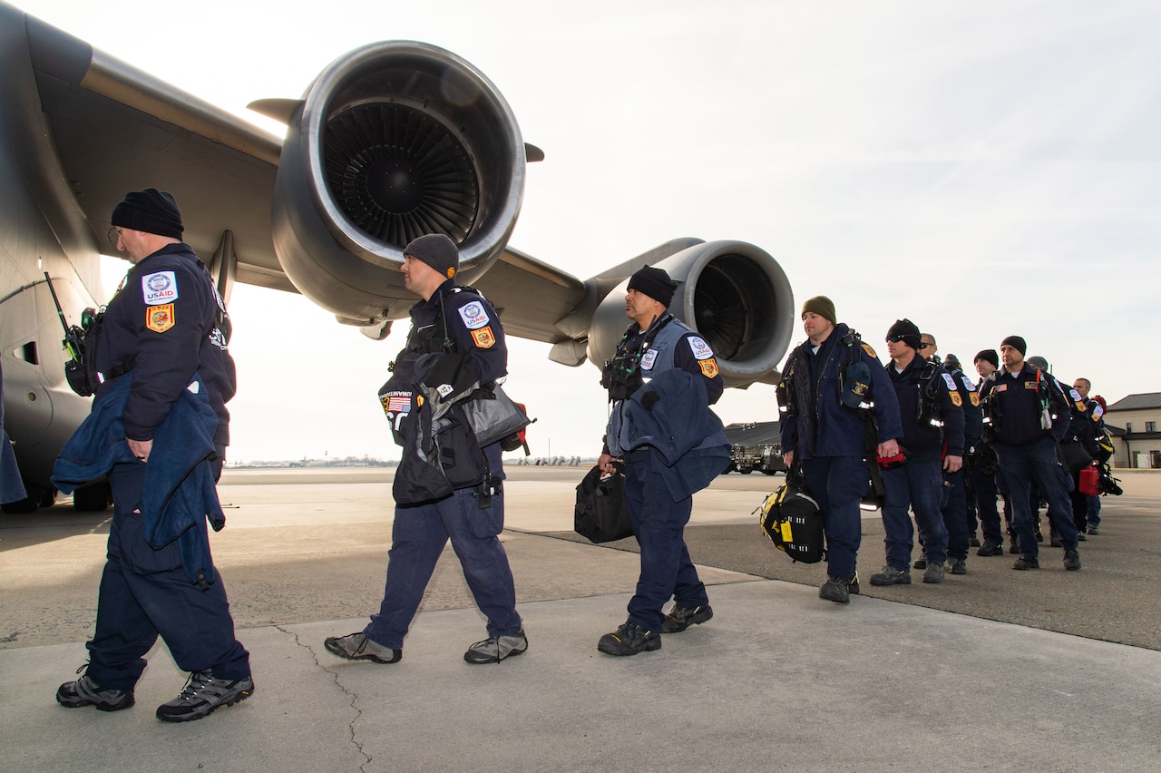 Rescue workers walk on a flight line toward a parked aircraft.