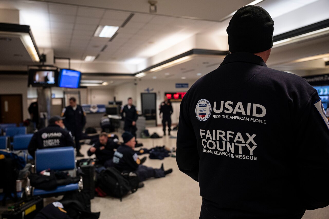 Civilian search and rescue personnel gather with baggage and gear in a waiting area.