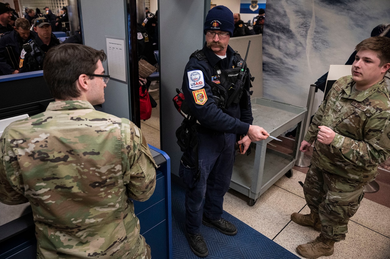 Two airmen stand and talk to a third person in a boarding area.