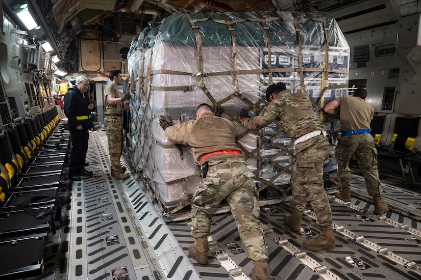 Three airmen push a pallet of cargo inside an aircraft.