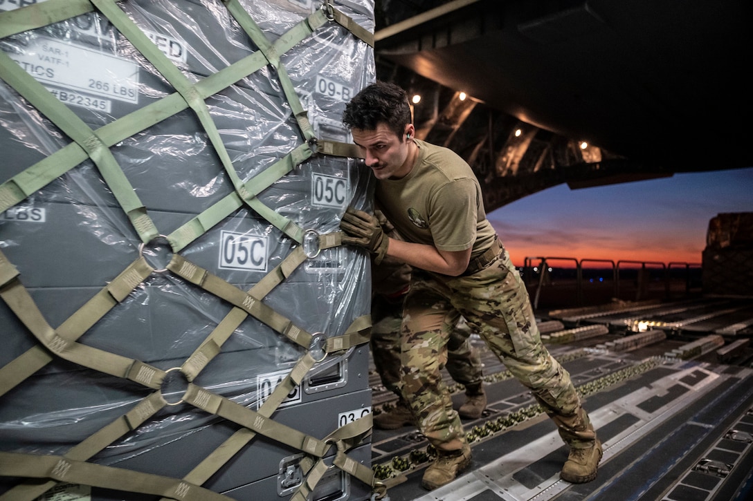 An airman  pushes cargo onto an aircraft.