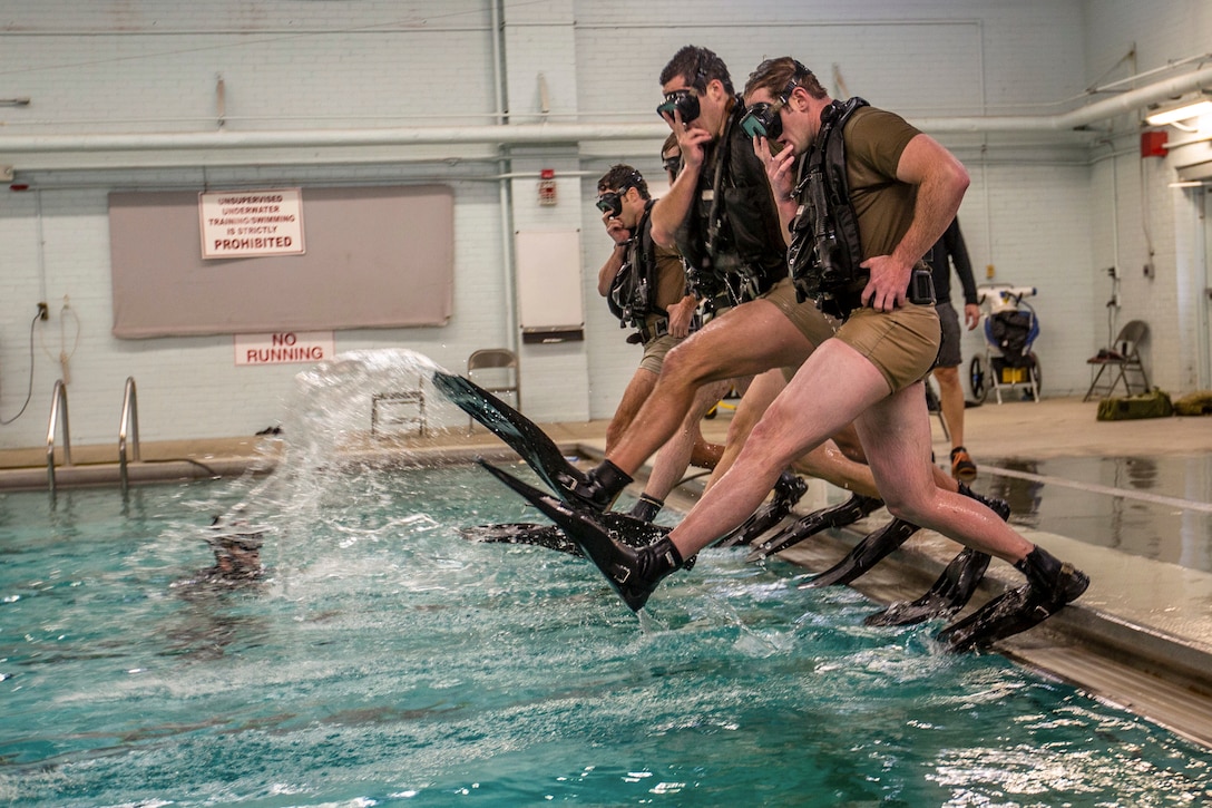 Soldiers wearing diving gear jump into a pool.