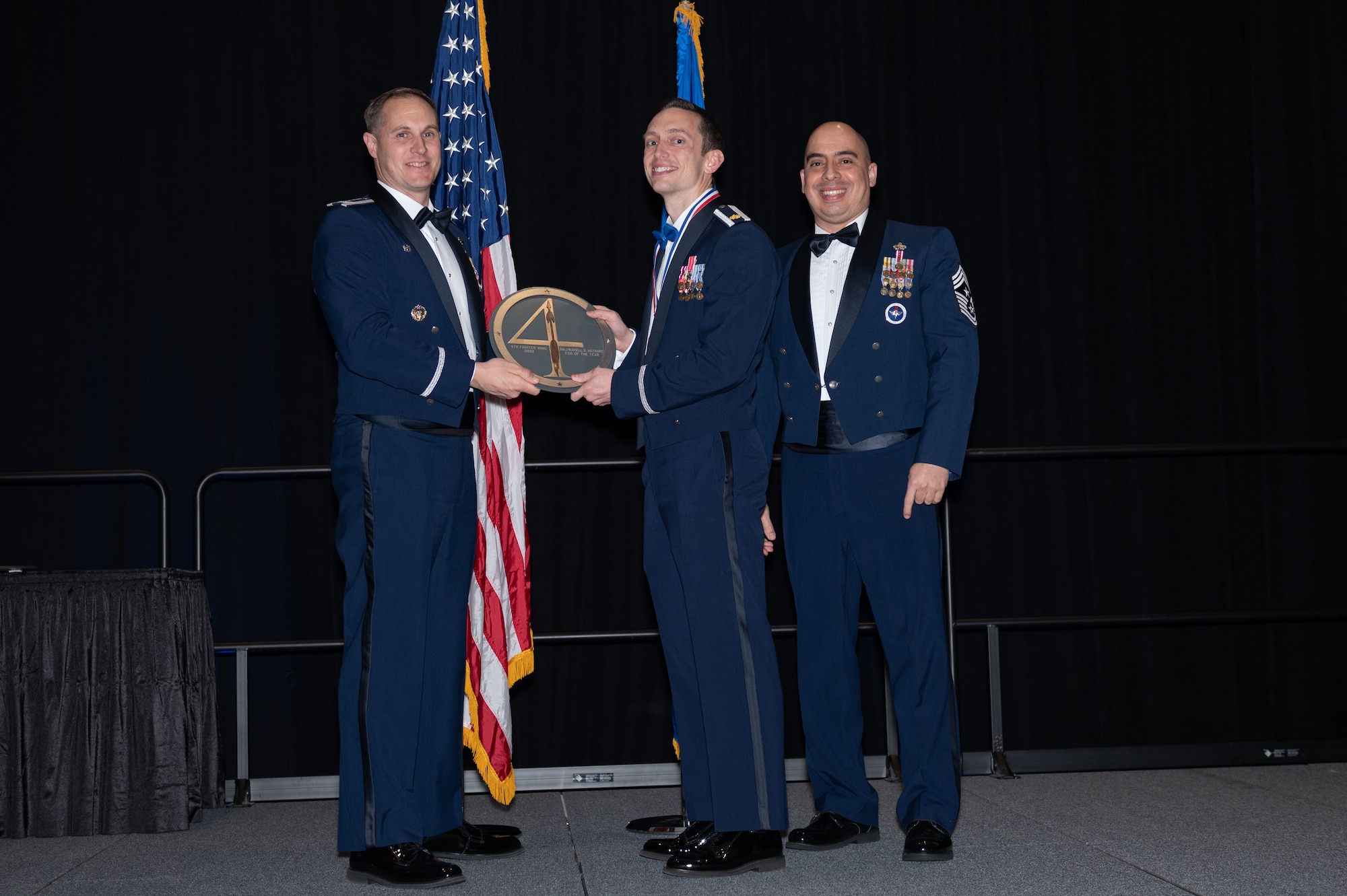 Maj. Russell Maynard, center, 4th Fighter Wing intelligence chief, receives the Field Grade Officer of the Year Award from Col. Lucas Teel, 4th Fighter Wing commander, and Chief Master Sgt. Peter Martinez, 4th FW command chief, during the 2022 Annual Awards ceremony at the Maxwell Center, Goldsboro, North Carolina, Feb. 3, 2023. Annual awards are awarded to Airmen and civilians in 13 different categories, including Volunteer of the Year, senior non-commissioned officer of the year, Key Spouse of the Year, Airman of the Year and more.  (U.S. Air Force photo by Rebecca Sirimarco-Lang)