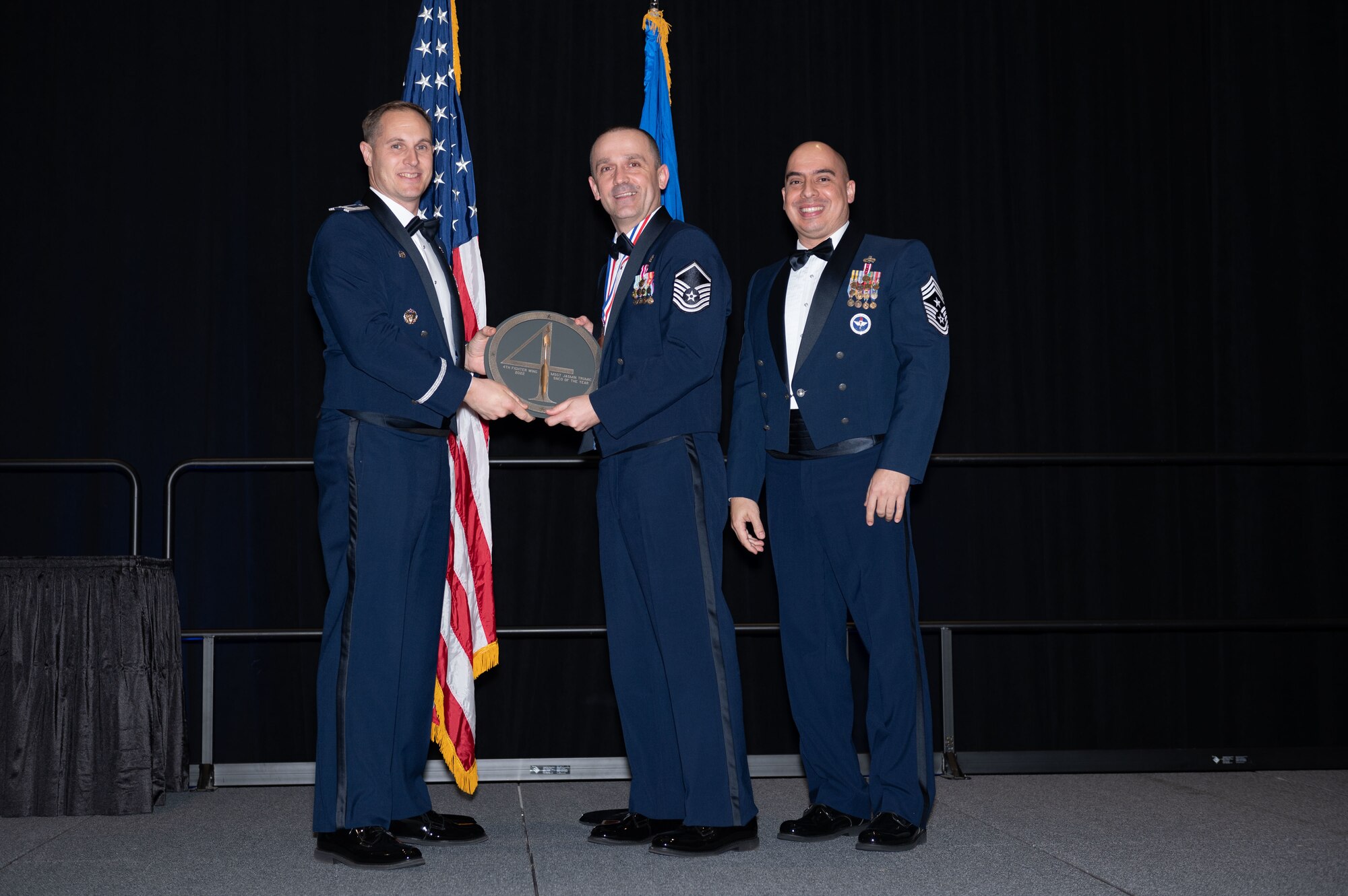 Master Sgt. Jasmin Trumic, center, 4th Healthcare Operations Squadron super intendent, receives the Senior Non-commissioned Officer of the Year Award from Col. Lucas Teel, 4th Fighter Wing commander, and Chief Master Sgt. Peter Martinez, 4th FW command chief, during the 2022 Annual Awards ceremony at the Maxwell Center, Goldsboro, North Carolina, Feb. 3, 2023. Annual awards are awarded to Airmen and civilians in 13 different categories, including Volunteer of the Year, senior non-commissioned officer of the year, Key Spouse of the Year, Airman of the Year and more. (U.S. Air Force photo by Rebecca Sirimarco-Lang)