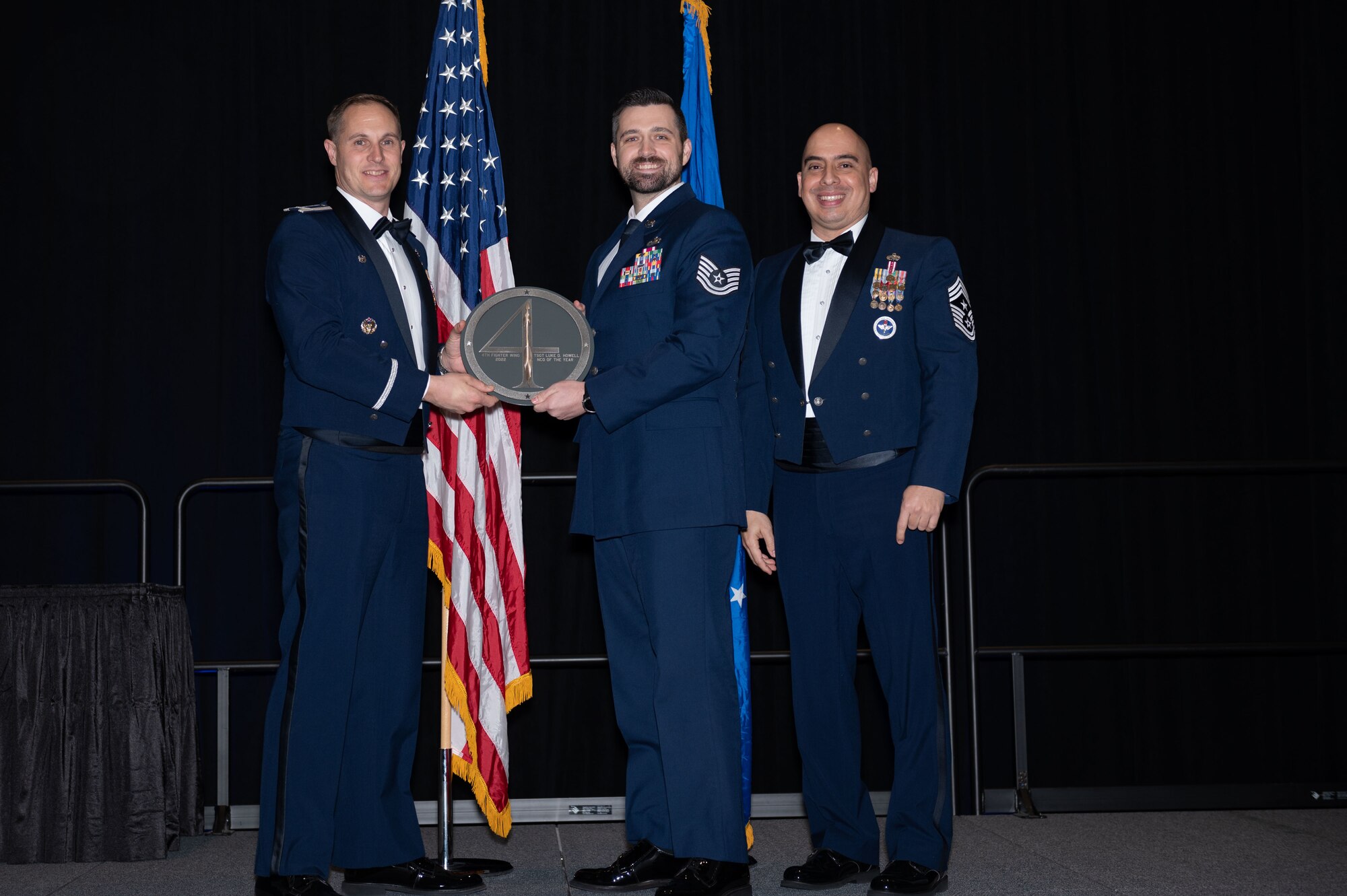 Tech Sgt. Luke Howell, center, 4th Operations Group section chief, receives the Non-commissioned Officer of the Year Award from Col. Lucas Teel, 4th Fighter Wing commander, and Chief Master Sgt. Peter Martinez, 4th FW command chief, during the 2022 Annual Awards ceremony at the Maxwell Center, Goldsboro, North Carolina, Feb. 3, 2023. Annual awards are awarded to Airmen and civilians in 13 different categories, including Volunteer of the Year, senior non-commissioned officer of the year, Key Spouse of the Year, Airman of the Year and more. (U.S. Air Force photo by Rebecca Sirimarco-Lang)
