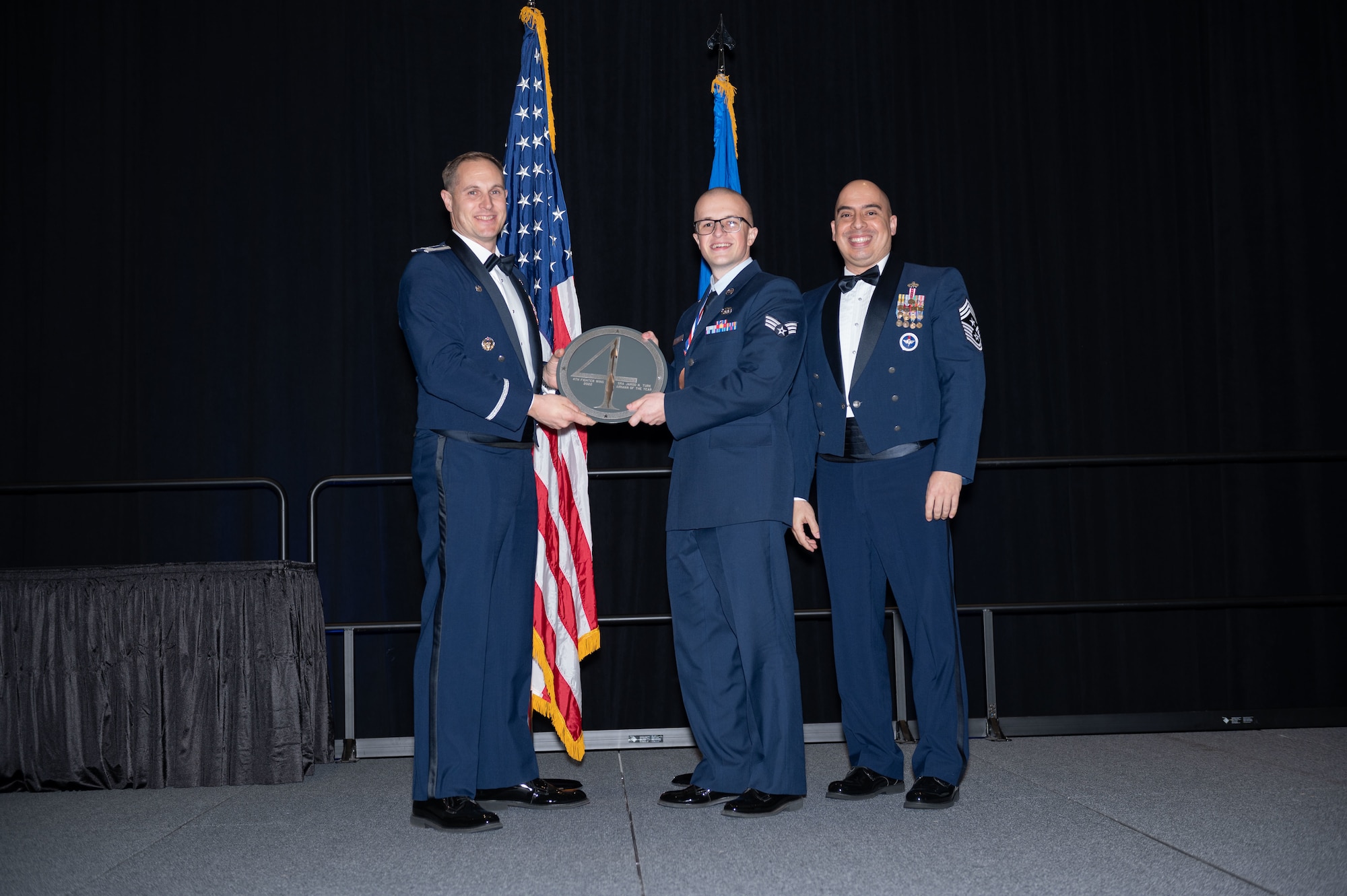 Senior Airman Jarod Turk, center, 4th Mission Support Group fuels equipment maintenance technician, receives the Airman of the Year Award from Col. Lucas Teel, 4th Fighter Wing commander, and Chief Master Sgt. Peter Martinez, 4th FW command chief, during the 2022 Annual Awards ceremony at the Maxwell Center, Goldsboro, North Carolina, Feb. 3, 2023. Annual awards are awarded to Airmen and civilians in 13 different categories, including Volunteer of the Year, senior non-commissioned officer of the year, Key Spouse of the Year, Airman of the Year and more.   (U.S. Air Force photo by Rebecca Sirimarco-Lang)
