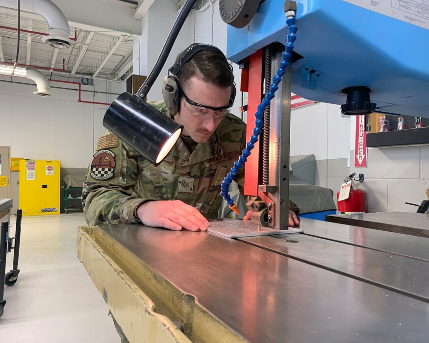 Uniformed male service member uses a table saw to cut metal.