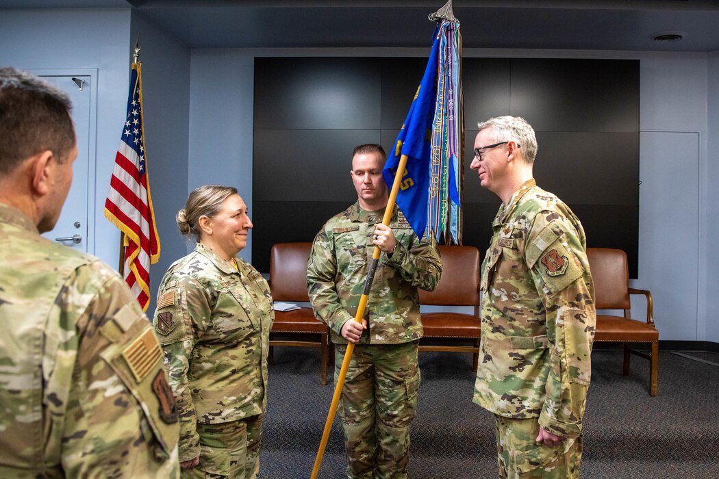 Female service member faces male servicemember with glasses while male servicemember holding unit guidon faces audience.