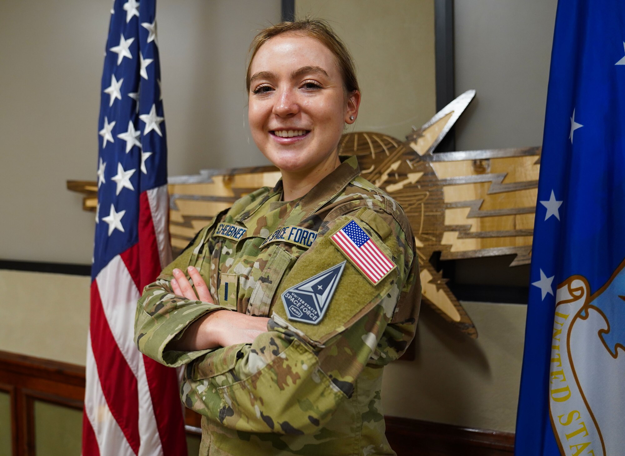 Portrait photo of 1st Lt. Katie Scheibner posing with her arms crossed in front of a U.S. flag and an Air Force flag.