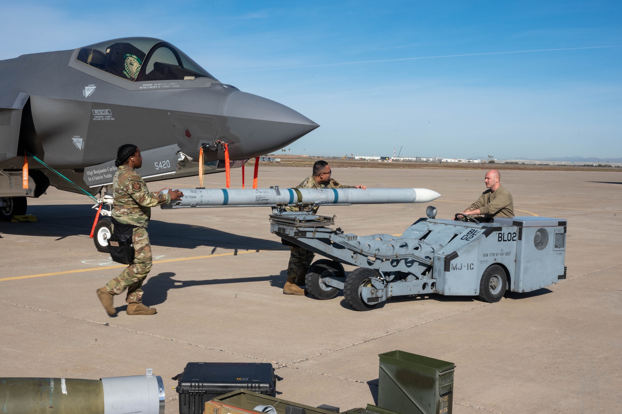 U.S. Air Force Staff Sgt. Emil Paclob, Senior Airman Janecia Peterson, and Senior Airman Cameron Canipe, 308th Aircraft Maintenance Unit maintainers, transport an AIM-120 AMRAAM missile during the annual weapons load competition Feb. 3, 2023, at Luke Air Force Base, Arizona.