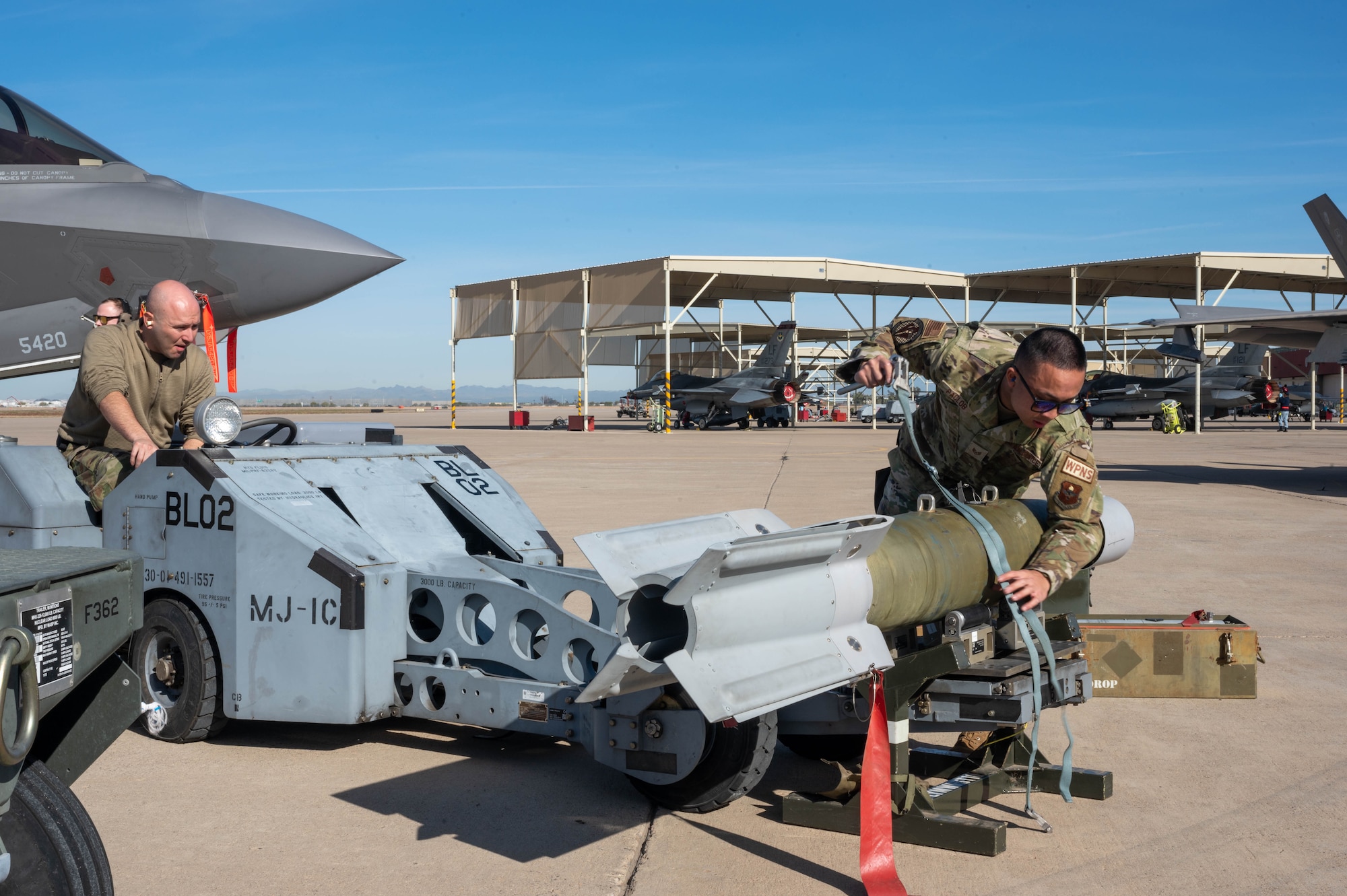 U.S. Air Force Staff Sgt. Emil Paclob and Senior Airman Cameron Canipe, 308th Aircraft Maintenance Unit maintainers, secure an GBU-12 Paveway II bomb during the annual weapons load competition Feb. 3, 2023, at Luke Air Force Base, Arizona.