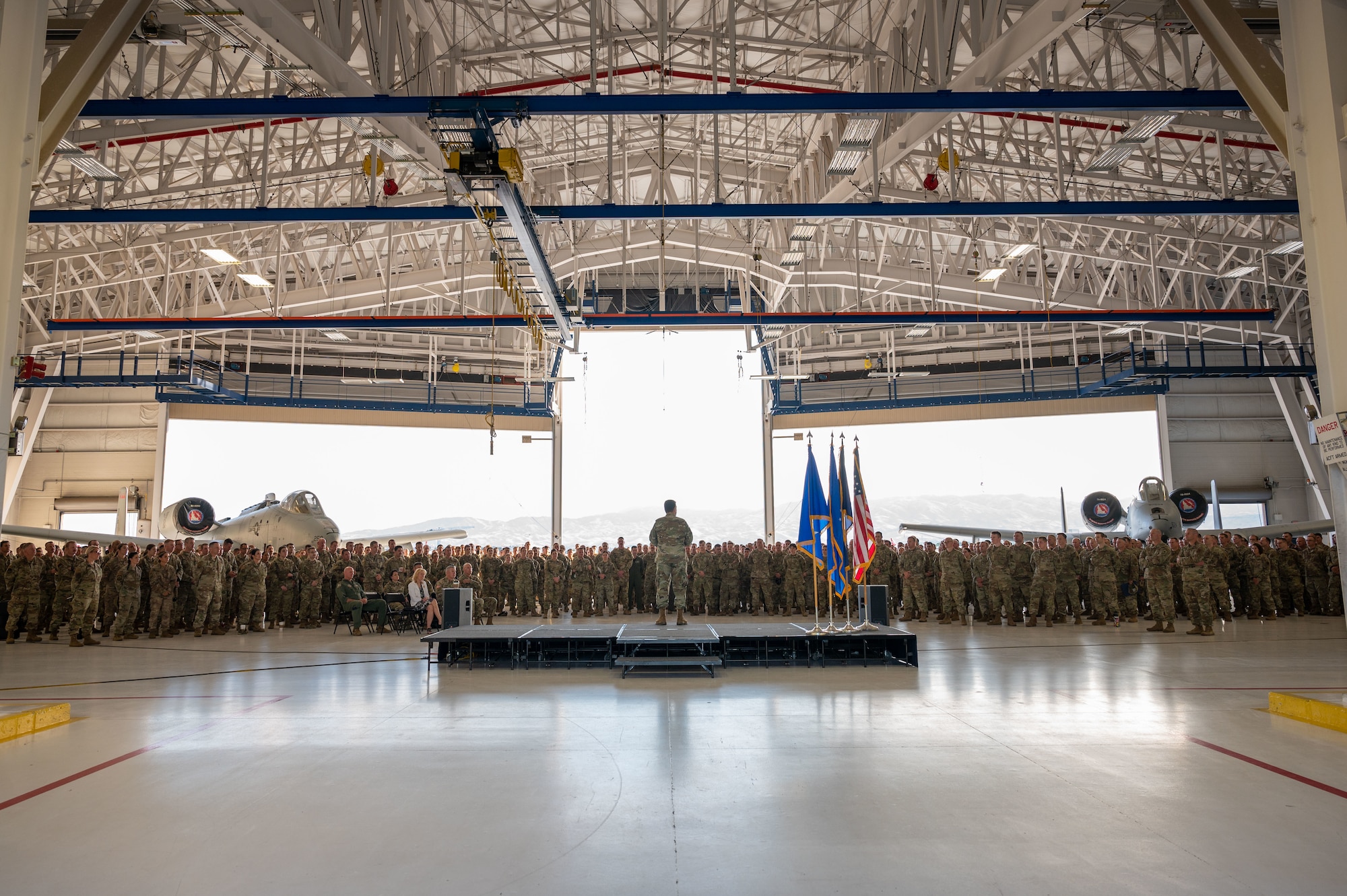 A picture of a hanger with the doors open and a crowd of Airmen on the hangar floor with two A-10 Thunderbolt IIs
