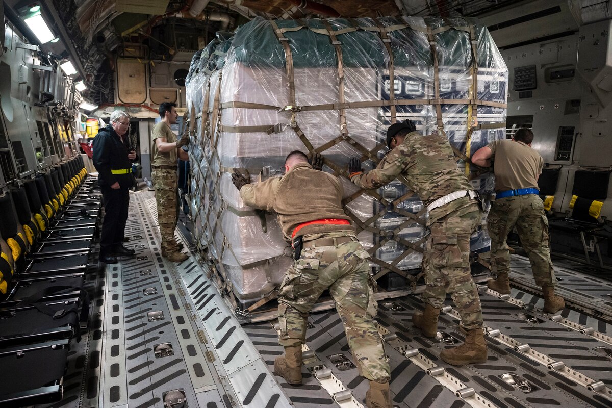 Three airmen push a pallet of cargo inside an aircraft.