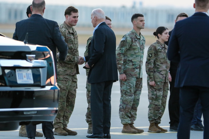 An older man dressed in civilian clothing shakes hands with a young soldier.