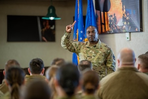 Chief Master Sgt speaks to airmen at an enlisted all call, people sitting in room while man is speaking