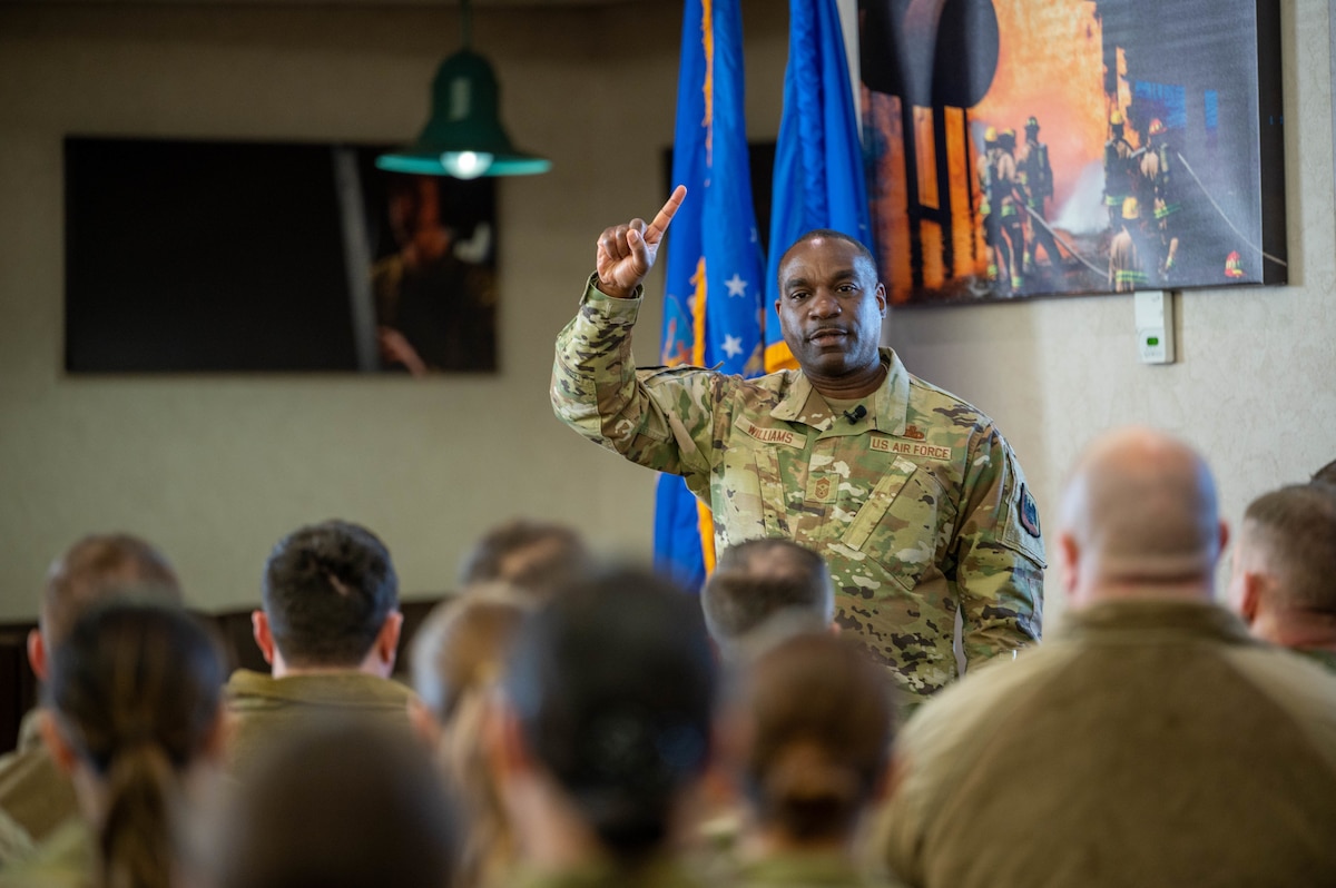Chief Master Sgt speaks to airmen at an enlisted all call, people sitting in room while man is speaking