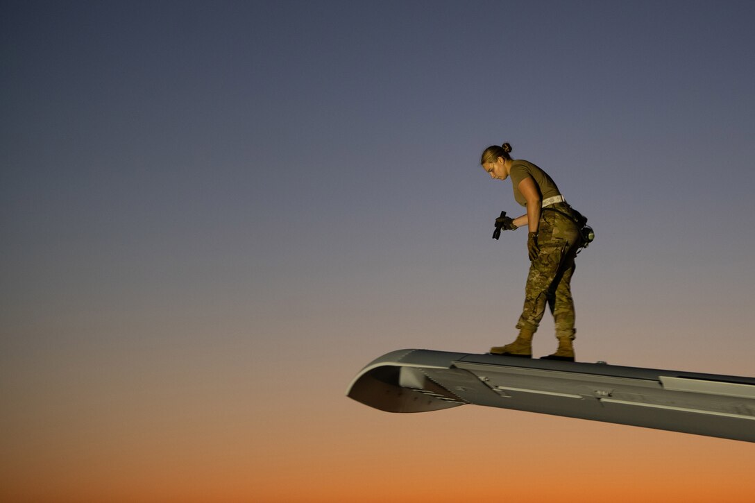A service member stands on the wing of a military aircraft to inspect it.