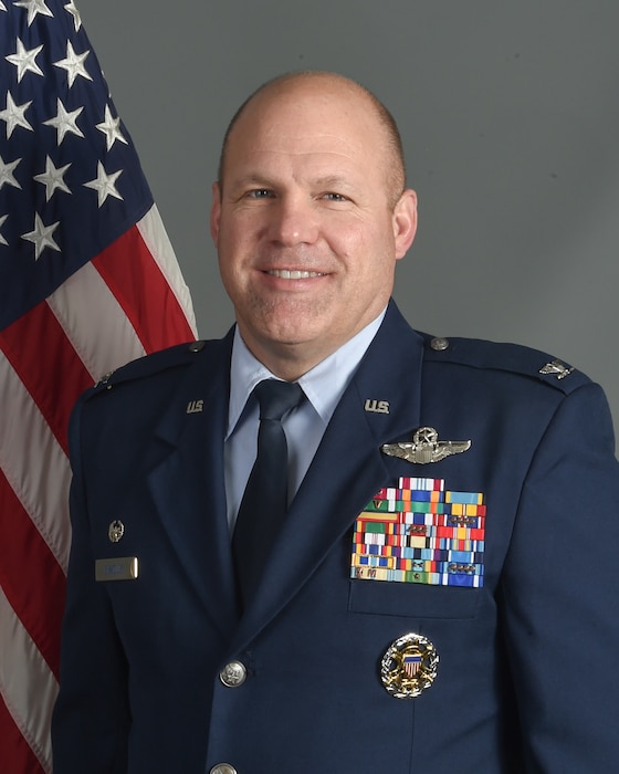 Man in blue uniform poses in front of US Flag