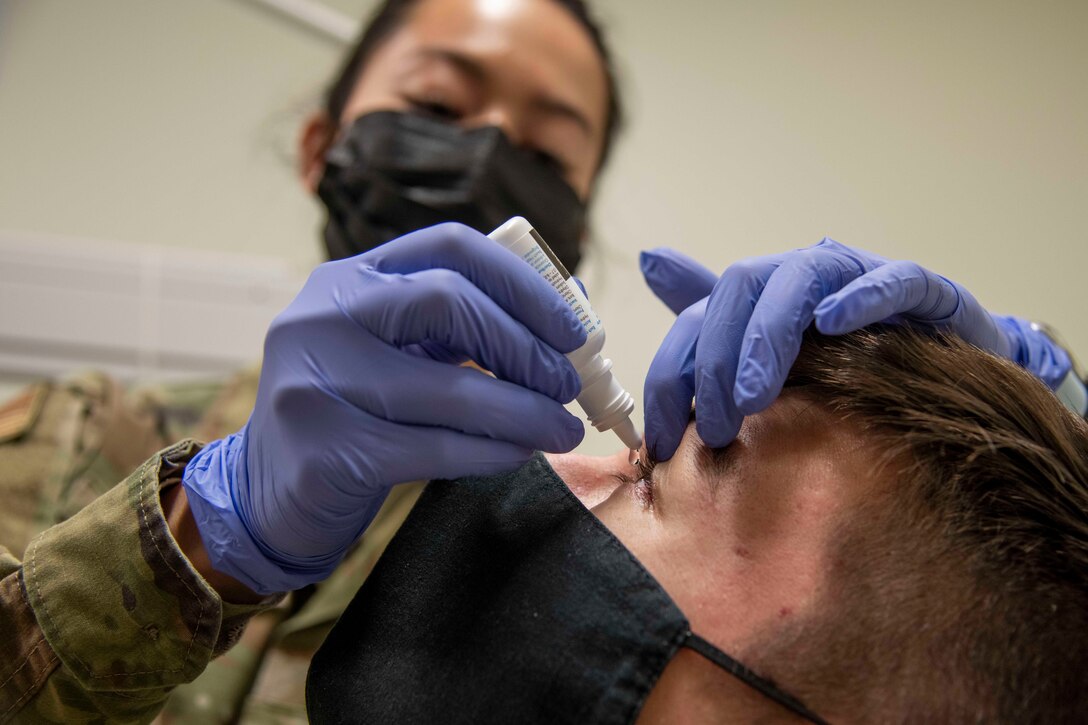 Close-up photo of a service member administering eye drops in a patient’s eyes.