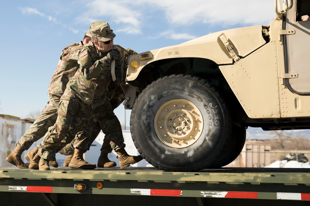 Soldiers push a vehicle off a flatbed truck.