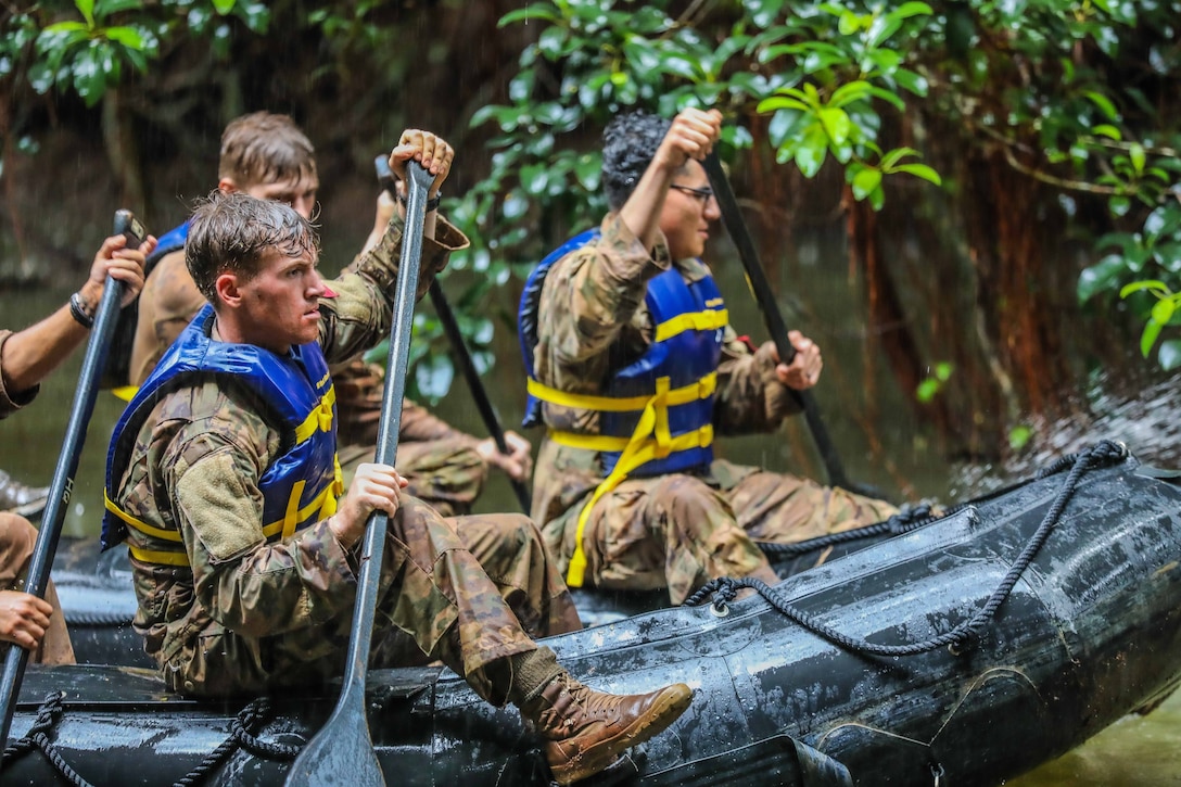 A group of soldiers paddle rubber rafts on a river.