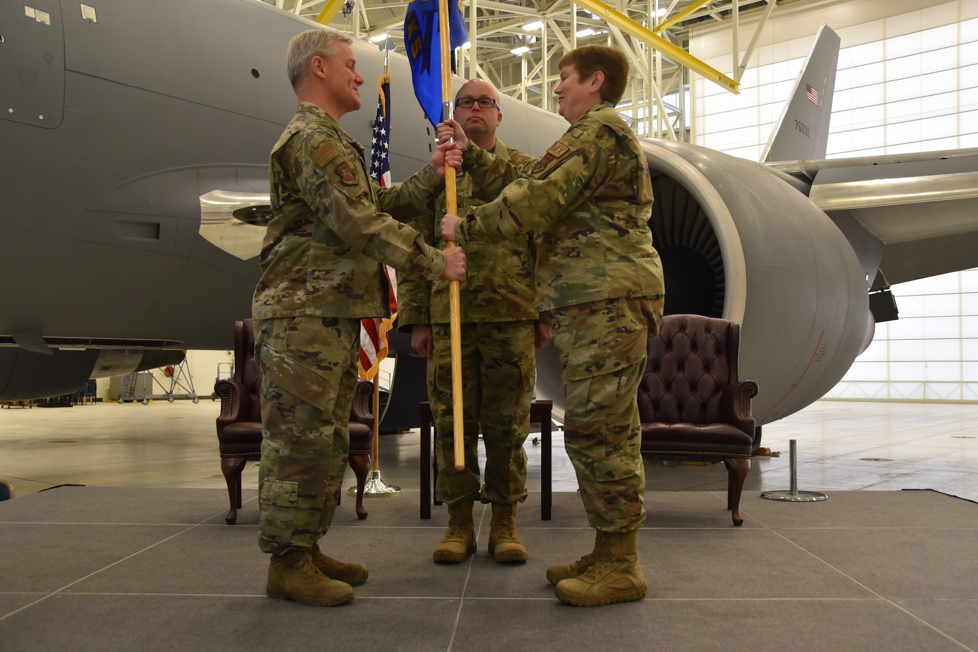 (Left to right) Lt. Col. Pamela Potter, incoming 931st Aircraft Maintenance Squadron commander, receives the guidon from Col. Robert Thompson, 931st Maintenance Group commander, on a stage in a hangar with a KC-46A Pegasus in the background.